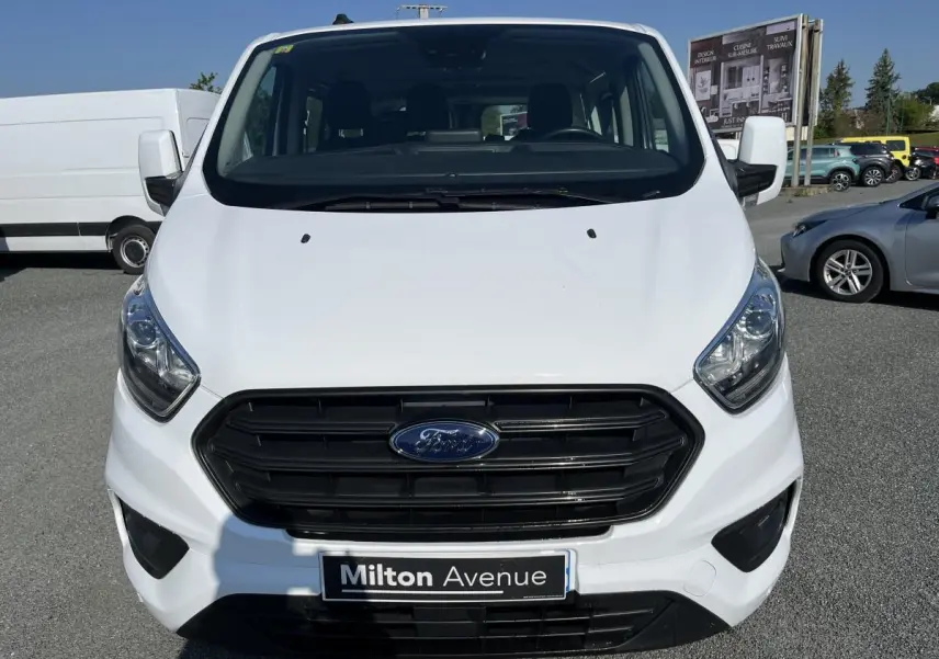 Vue frontale d'un Ford Transit Custom Kombi blanc avec calandre noire et plaque Milton Avenue visible.