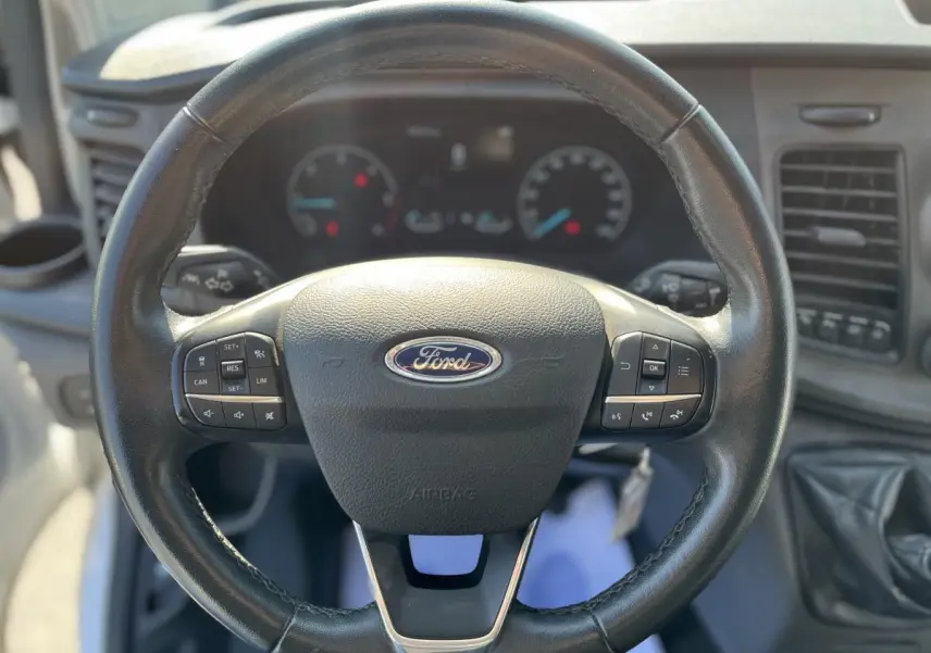 Volant en cuir noir de Ford Transit Custom 2021 avec commandes intégrées et tableau de bord en arrière-plan flou.