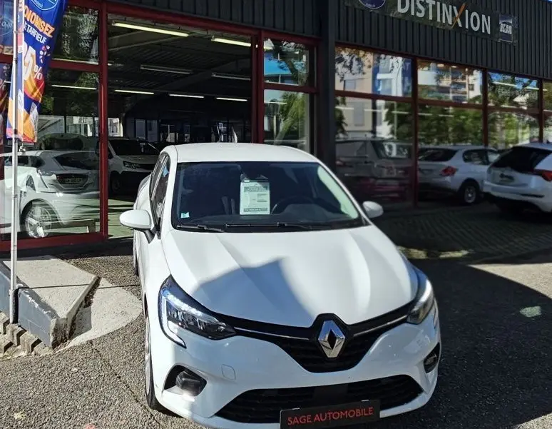 Renault Clio blanc glacier vue de face, stationnée devant un garage avec enseigne AD Expert.