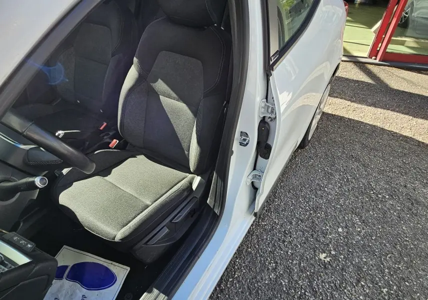 Vue intérieure côté conducteur d'une Renault Clio blanche glacier 2021, sièges noirs en tissu et tableau de bord visible.