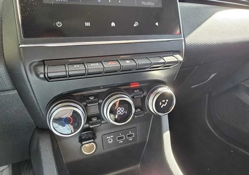 Vue rapprochée de la console centrale de la Renault Clio blanche, mettant en valeur les commandes de climatisation et les boutons de fonction.