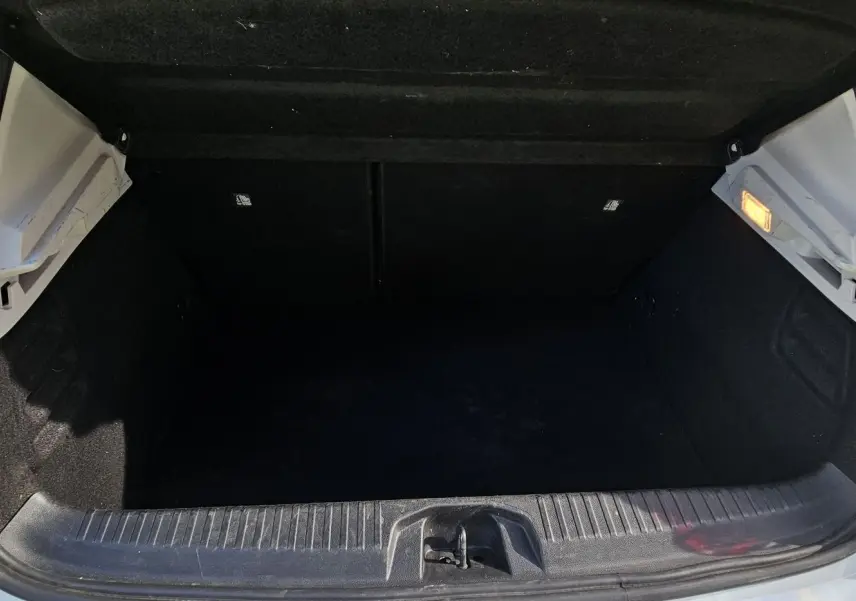 Coffre ouvert vu de l'arrière d'une Renault Clio blanche Glacier hybride, montrant l'espace de chargement vide et l'éclairage intérieur.