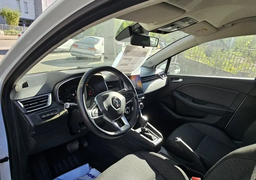 Intérieur de la Renault Clio blanc glacier 2021, vue côté conducteur, tableau de bord moderne avec écran tactile et volant multifonction.