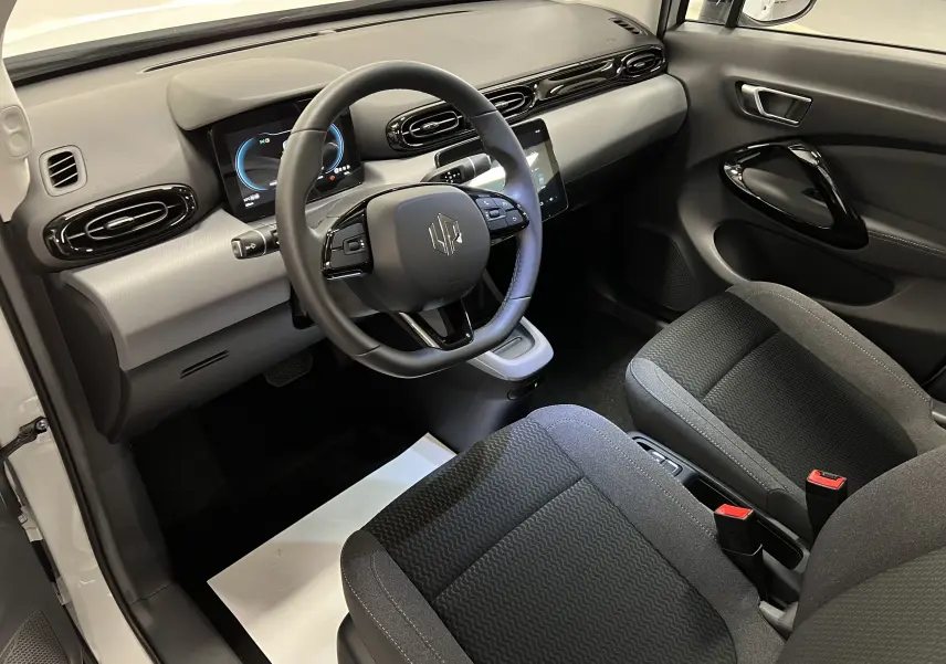 Intérieur de la Renault ZOE blanc 2024, vue côté conducteur, tableau de bord moderne avec écran digital et sièges tissu noirs.