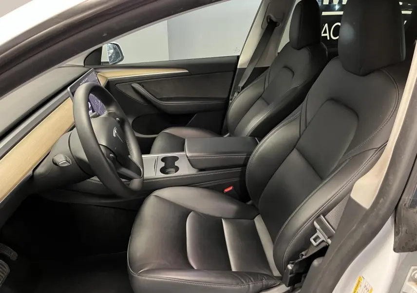 Intérieur noir de la Tesla Model Y RWD 2022 vu côté conducteur, avec tableau de bord bois clair et volant multifonction.