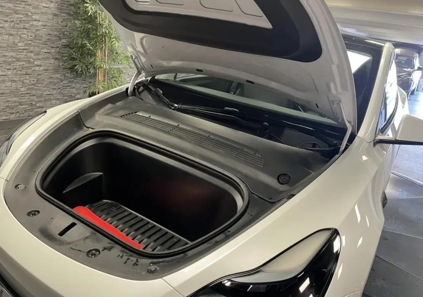 Vue 3/4 avant droit d'une Tesla Model Y blanche avec capot ouvert dévoilant le coffre avant vide.