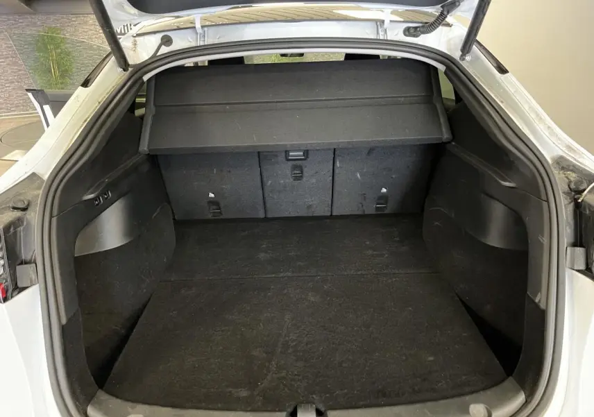 Coffre ouvert d'une Tesla Model Y blanc nacré, montrant l'espace de chargement et la tablette de séparation noire.