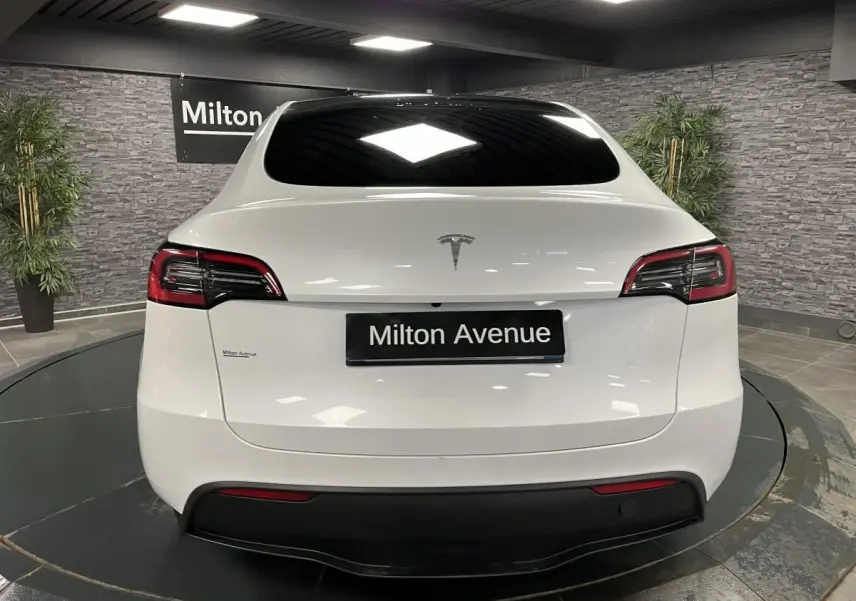 Vue arrière d'une Tesla Model Y blanche nacrée avec vitres teintées et logo Tesla visible sur le hayon.