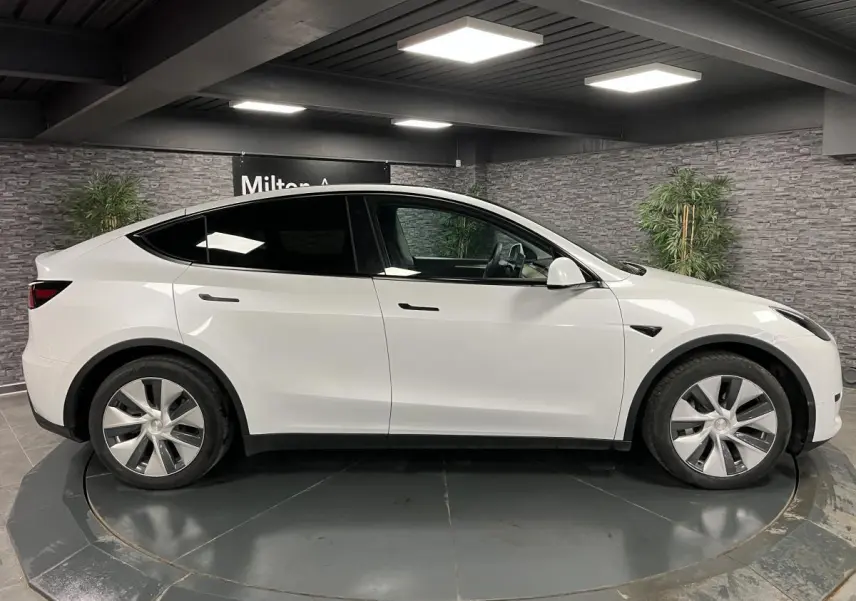 Profil côté gauche d'une Tesla Model Y blanche 2022 RWD Autonomie Standard en intérieur avec jantes alu.