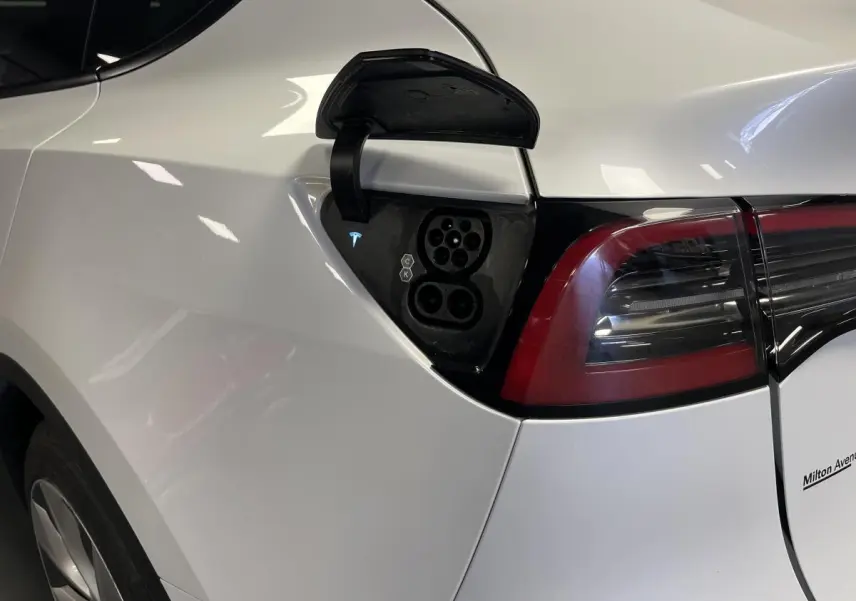 Prise de recharge ouverte côté gauche arrière d'une Tesla Model Y blanche avec feux arrière LED visibles.