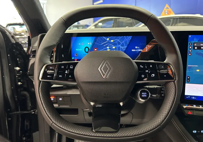 Vue frontale du volant noir du Renault Austral Ph.2 E-TECH avec commandes intégrées et écran numérique en arrière-plan.