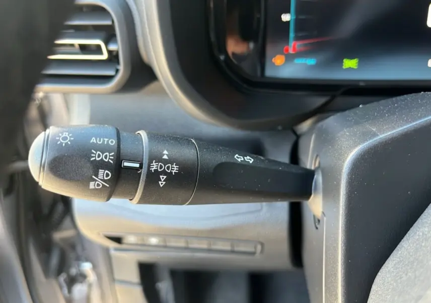 Gros plan sur la manette de commande des feux du Citroën Berlingo 2025, intérieur noir avec tableau de bord numérique.