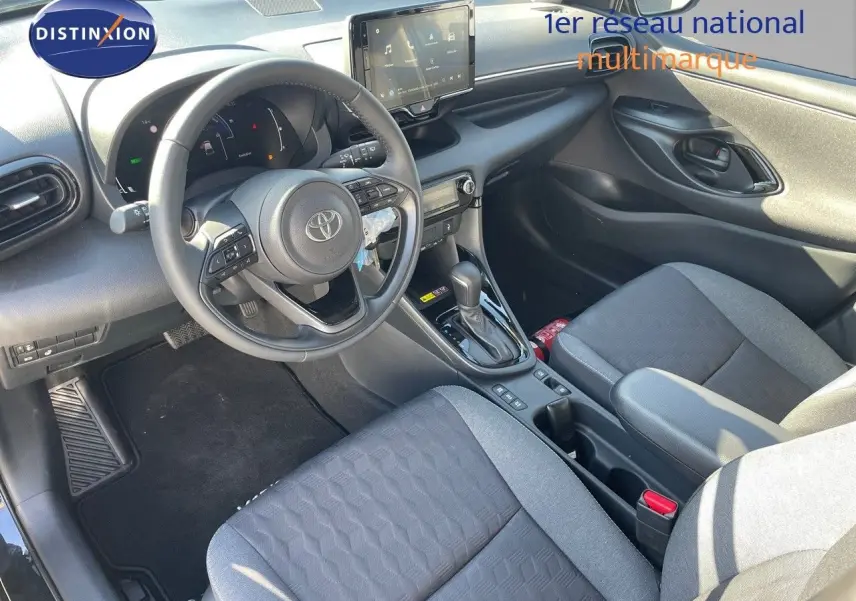 Intérieur de la Toyota Yaris Hybrid 2025 vu côté conducteur, avec tableau de bord noir et sièges tissu gris.
