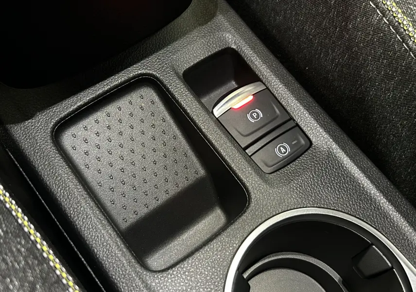 Gros plan sur la console centrale noire étoilé du Renault Captur II Ph.2 TECHNO avec bouton frein à main électrique allumé.