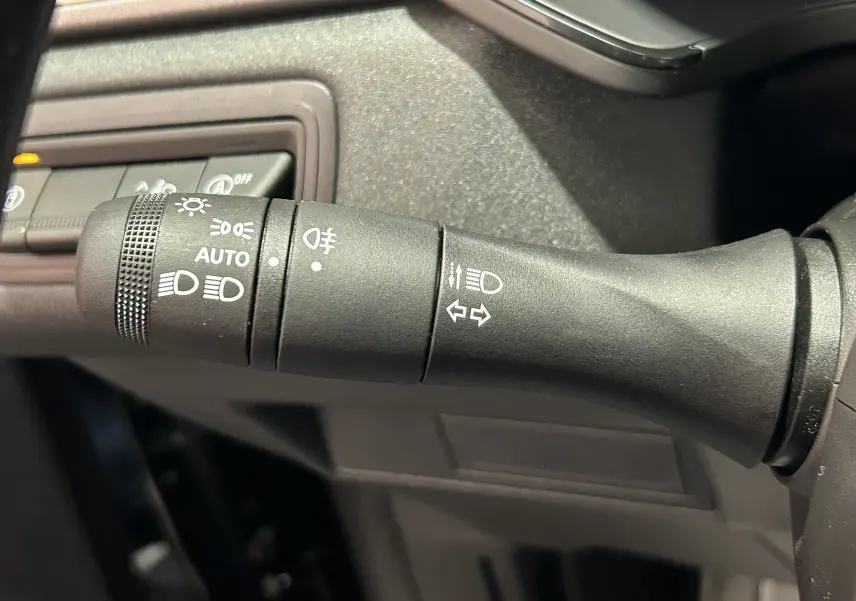 Gros plan sur la commande des phares et clignotants du Renault Captur II Ph.2 TECHNO noir étoilé, intérieur sombre.