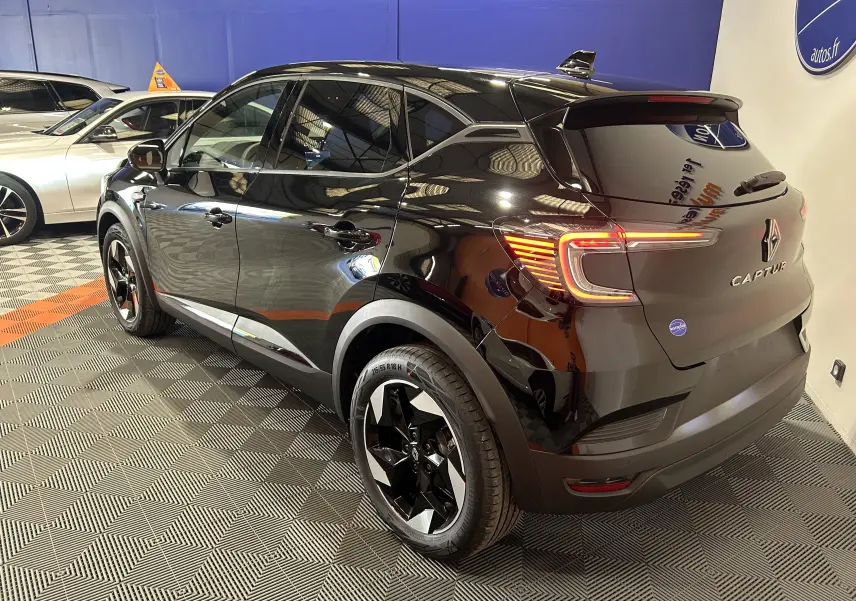 Renault Captur II Ph.2 TECHNO noir étoilé vu en 3/4 arrière droit, avec feux arrière allumés et jantes bicolores.