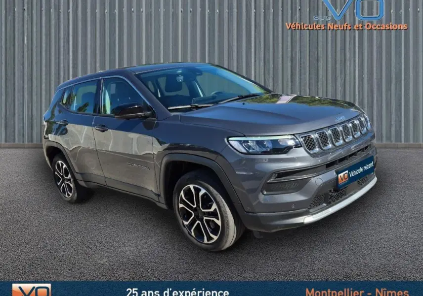 Jeep Compass gris 3/4 avant droit avec jantes alliage 18 pouces, stationné devant un mur métallique.