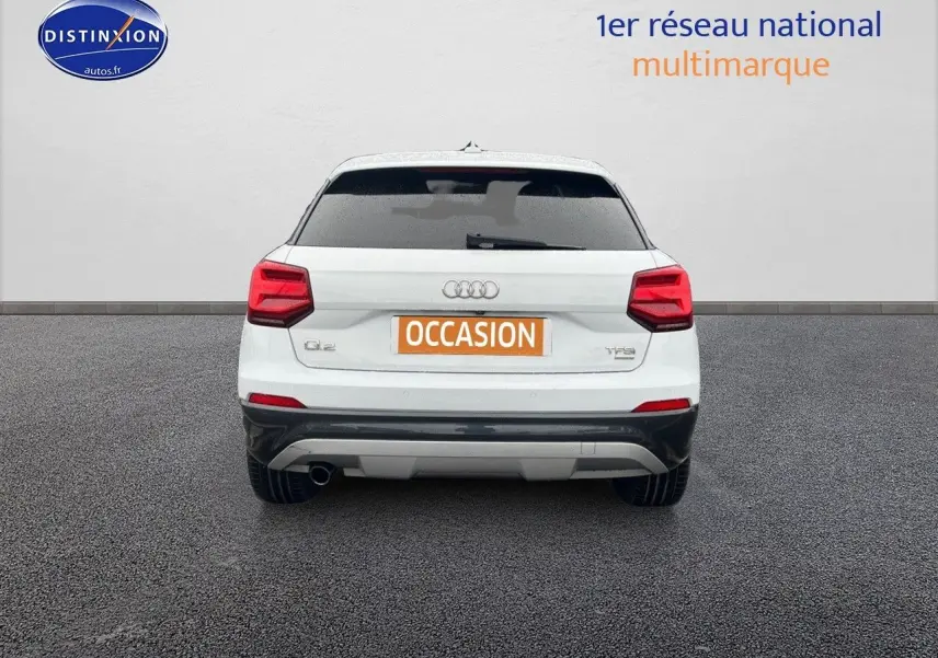 Vue arrière d'un Audi Q2 blanc Ibis avec feux rouges et pare-chocs noir, sur fond gris neutre.