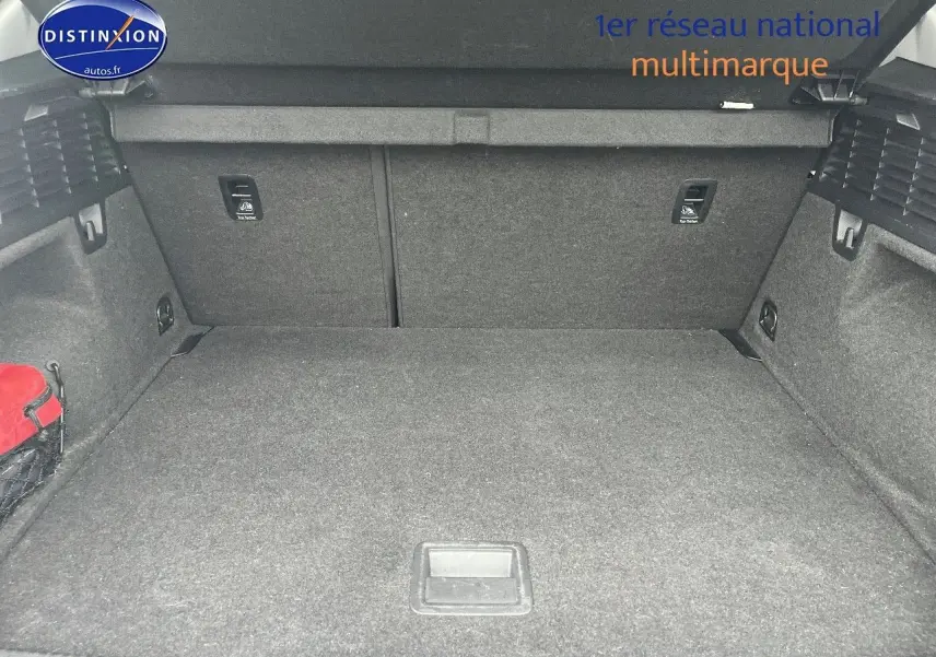 Coffre spacieux de l'Audi Q2 blanc Ibis vu de face, avec revêtement gris et filet de rangement latéral rouge.