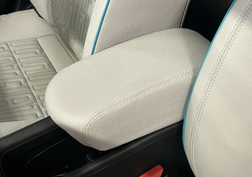 Gros plan sur l'accoudoir beige et les sièges en cuir clair avec surpiqûres bleues de la Fiat 600 Hybrid 2024.