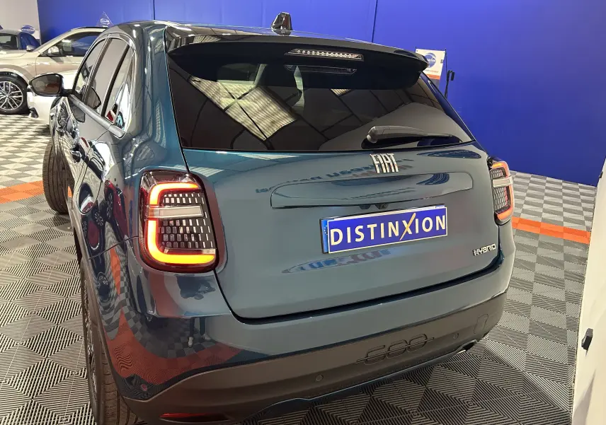 Vue 3/4 arrière d'une FIAT 600 Hybrid bleu avec hayon électrique et feux arrière LED allumés dans un showroom.