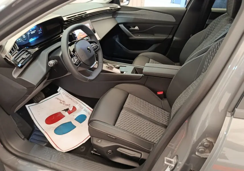 Intérieur avant droit de la Peugeot 308 gris foncé 2026, volant cuir multifonctions et sièges tissu/cuir bicolores.