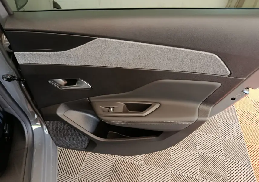 Vue intérieure côté gauche de la porte avant gris foncé de la Peugeot 308 2026 avec garniture tissu et commandes électriques.