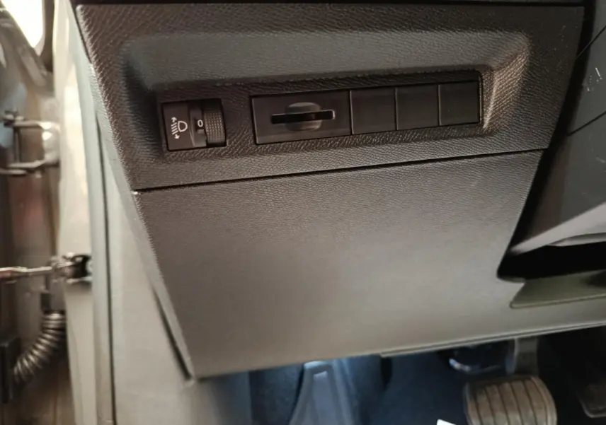 Vue rapprochée du panneau de réglage des phares et interrupteurs sur le côté gauche du tableau de bord gris foncé d’une Peugeot 308 2026.