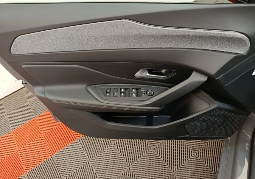 Vue intérieure côté gauche de la porte avant d'une Peugeot 308 gris foncé avec commandes électriques et insert tissu gris.