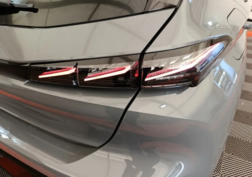 Feu arrière droit allumé en détail sur Peugeot 308 gris foncé, vue rapprochée du coin arrière du véhicule.