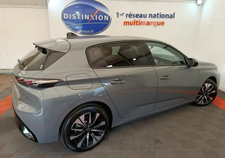 Peugeot 308 BlueHDi 130 en gris foncé, vue 3/4 arrière côté droit, avec jantes noires et feux LED distinctifs.