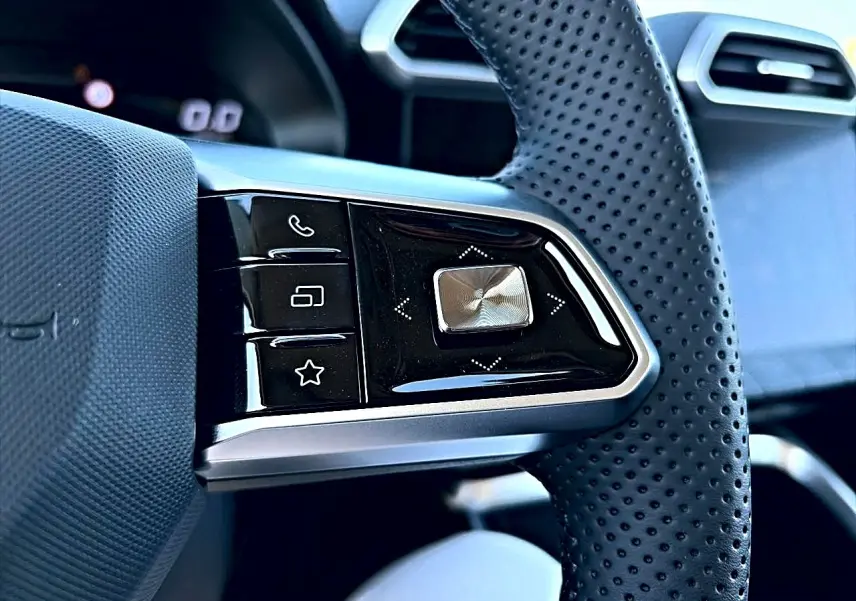 Gros plan sur les commandes multifonctions noires et argent du volant perforé du MG Motor ZS hybride noir, intérieur moderne.