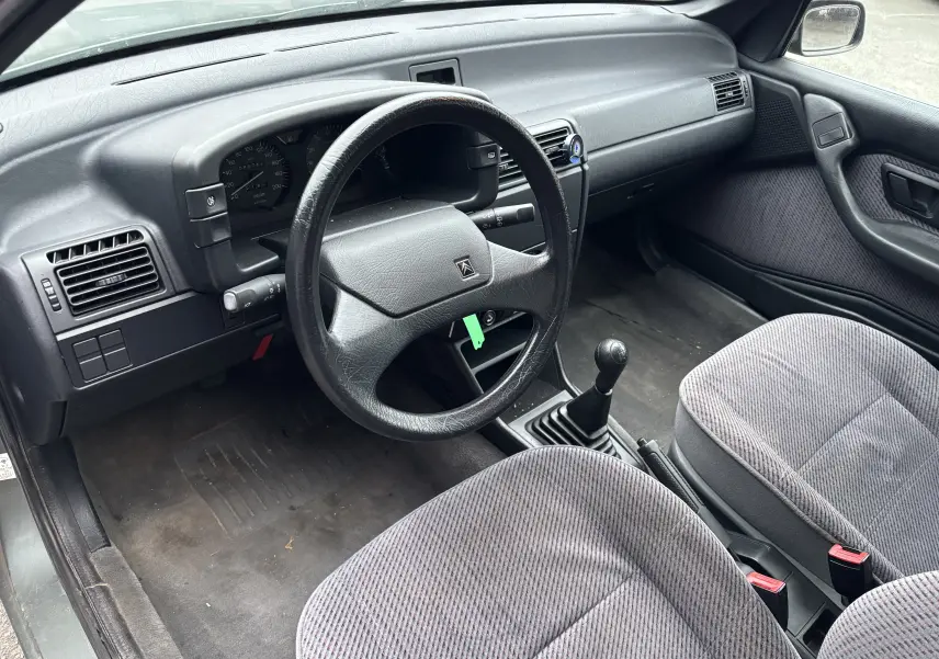 Intérieur côté conducteur de Citroën ZX 1.6i gris 1992, volant cuir, tableau de bord simple et sièges tissu rayé.