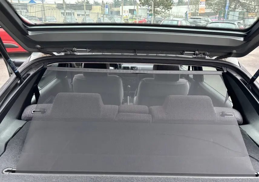 Vue arrière ouverte sur l'intérieur gris en tissu d'une Citroën ZX 1.6i 89CV de 1992 avec cache-bagages déployé.