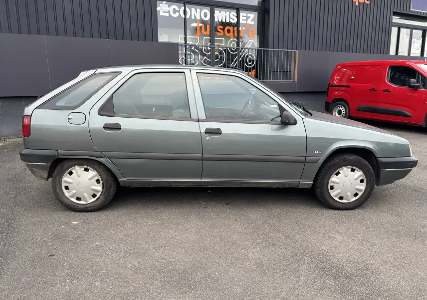 Profil côté gauche d'une Citroën ZX gris 1.6i 89CV de 1992 avec jantes acier et rétroviseurs noirs.