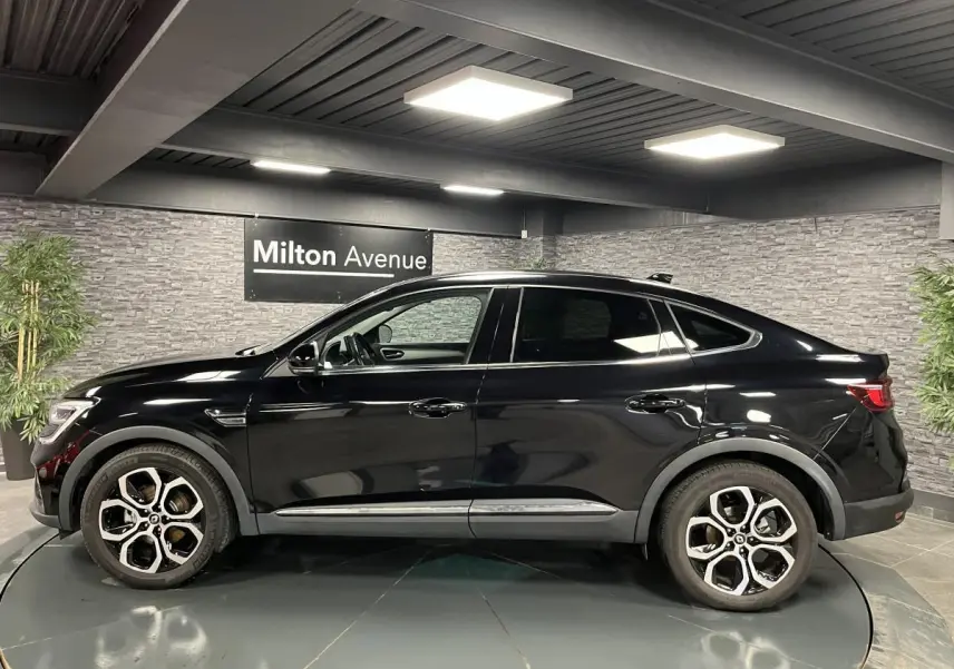 Profil côté gauche du Renault Arkana noir métal 2021 avec jantes alliage 18 pouces dans un showroom intérieur.