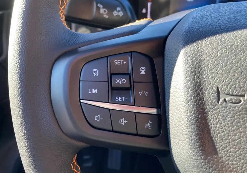 Gros plan sur les commandes multifonctions noires du volant cuir du Ford Ranger Wildtrak blanc glacier 2025.