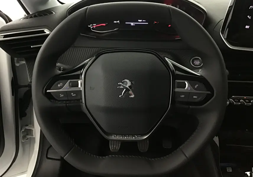 Vue rapprochée du volant noir de la Peugeot 208 blanche 2024 avec commandes intégrées et tableau de bord digital.