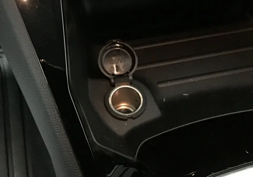 Prise 12V ouverte sur la console centrale noire d'une Peugeot 208 blanche essence 2024, version Allure Pack.