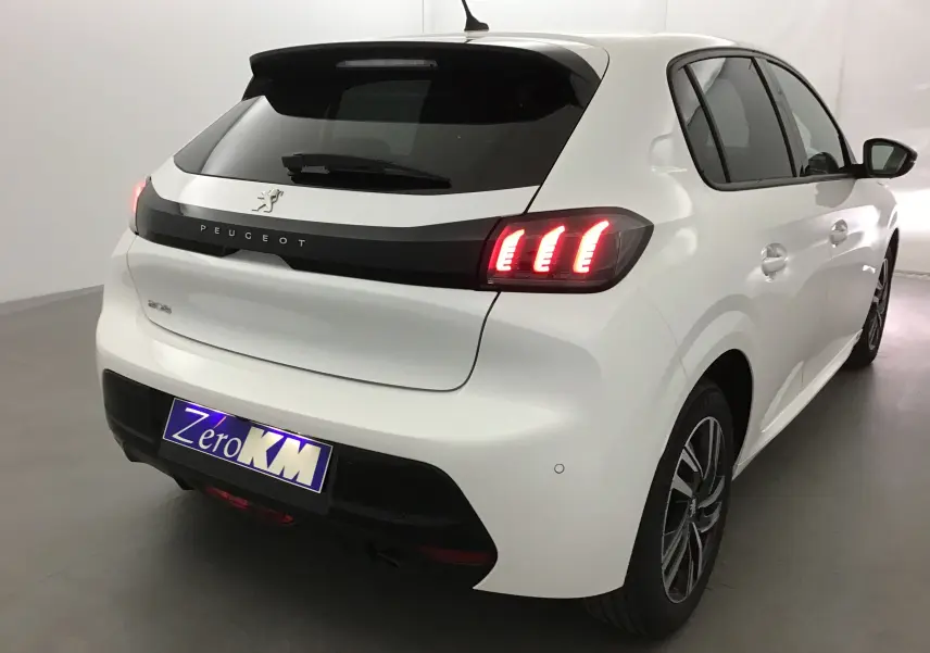 Vue 3/4 arrière droite d'une Peugeot 208 blanche 2024 avec feux arrière allumés et jantes alliage noires.