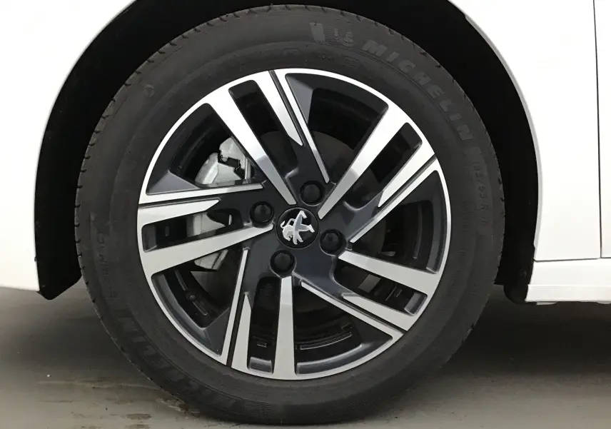 Gros plan sur la roue avant gauche blanche d'une Peugeot 208 1.2 PureTech 100 Allure Pack avec jante alliage noire et argent.