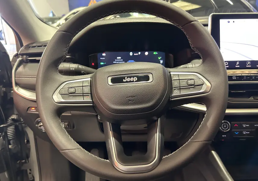 Volant en cuir noir avec logo Jeep au centre, tableau de bord numérique et écran tactile à droite dans un Jeep Compass gris 2021.