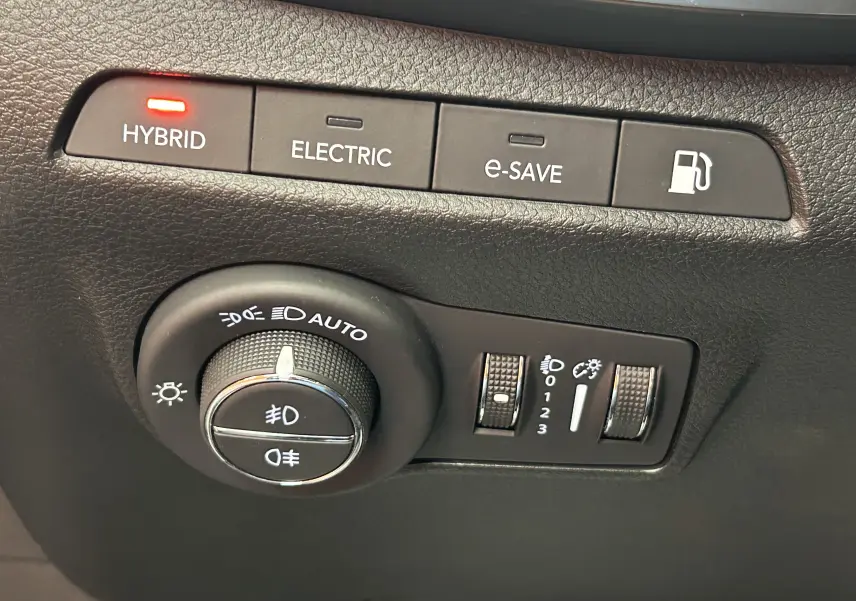 Vue rapprochée des commandes de modes hybrides et des réglages d'éclairage sur le tableau de bord noir du Jeep Compass gris.