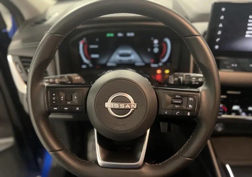 Volant cuir noir de Nissan Qashqai 1.3 Mild Hybrid 140 Shadow avec commandes intégrées et tableau de bord numérique flou.