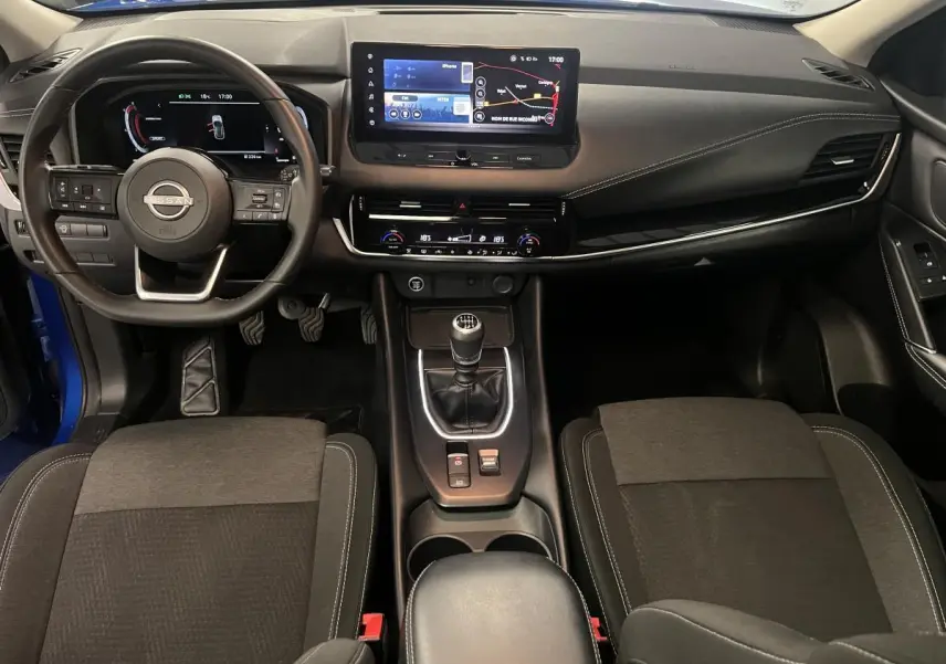 Intérieur avant du Nissan Qashqai 2024 bleu, vue du tableau de bord avec écran tactile et levier de vitesses manuel.