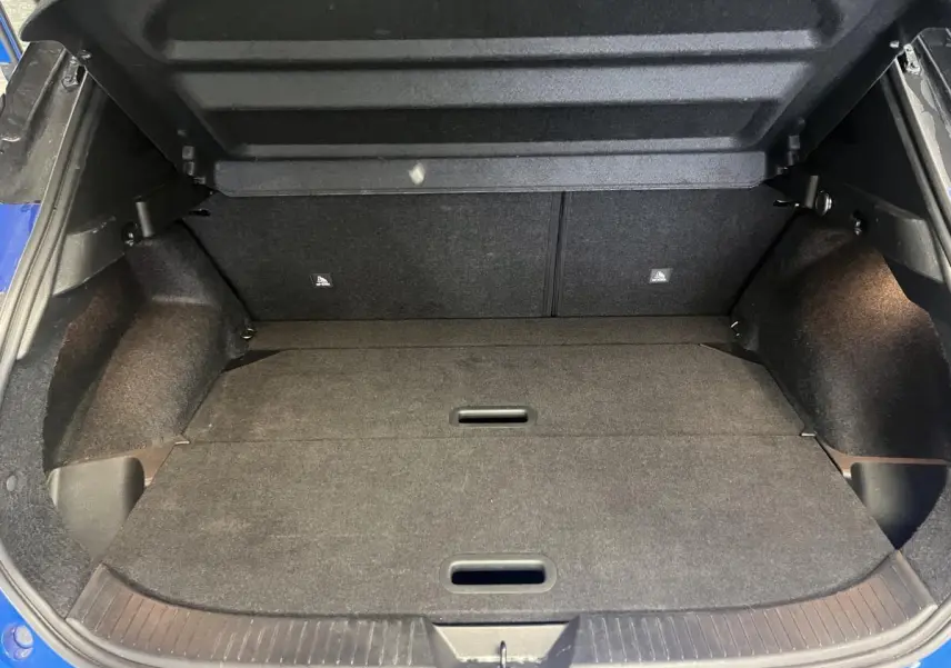 Coffre ouvert du Nissan Qashqai bleu 2024, vue arrière montrant le plancher plat et les parois intérieures noires.