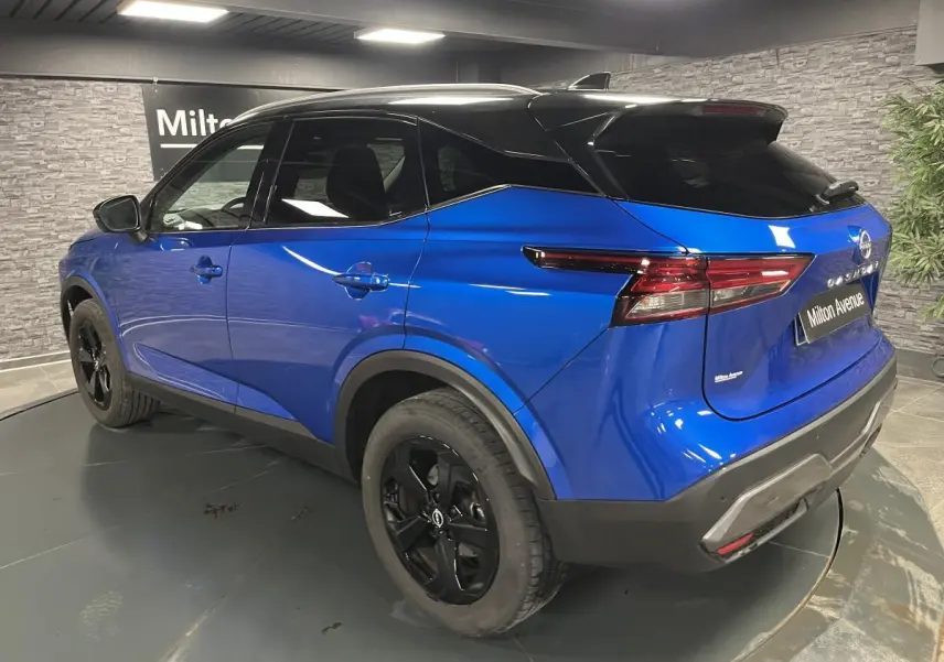 Vue 3/4 arrière droite du Nissan Qashqai 2024 bleu avec toit noir et jantes alliage noires en intérieur showroom.