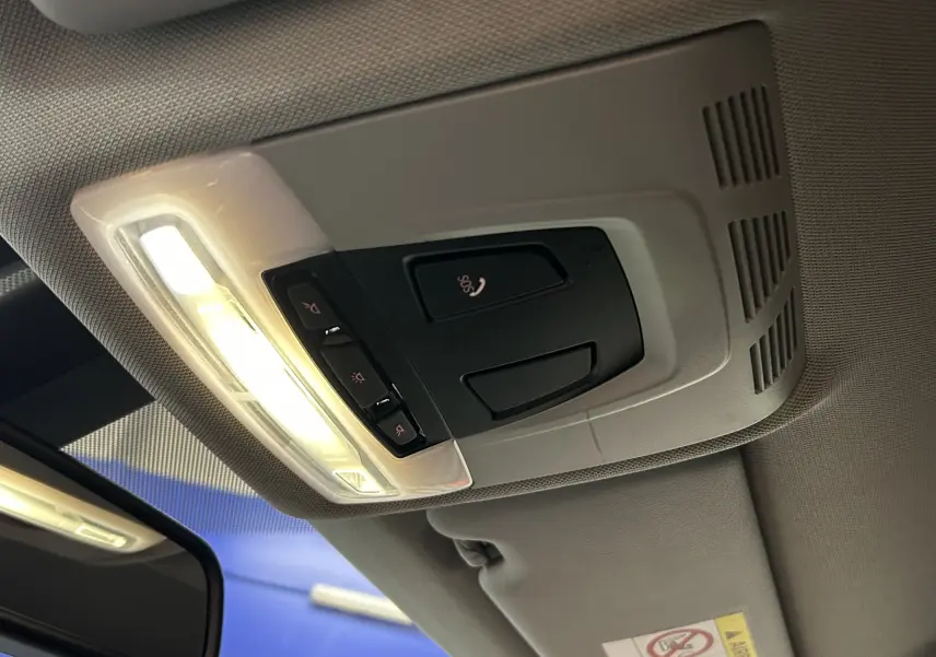 Vue intérieure du plafonnier avant de la BMW Série 3 320i blanc, avec éclairage et commandes SOS visibles.