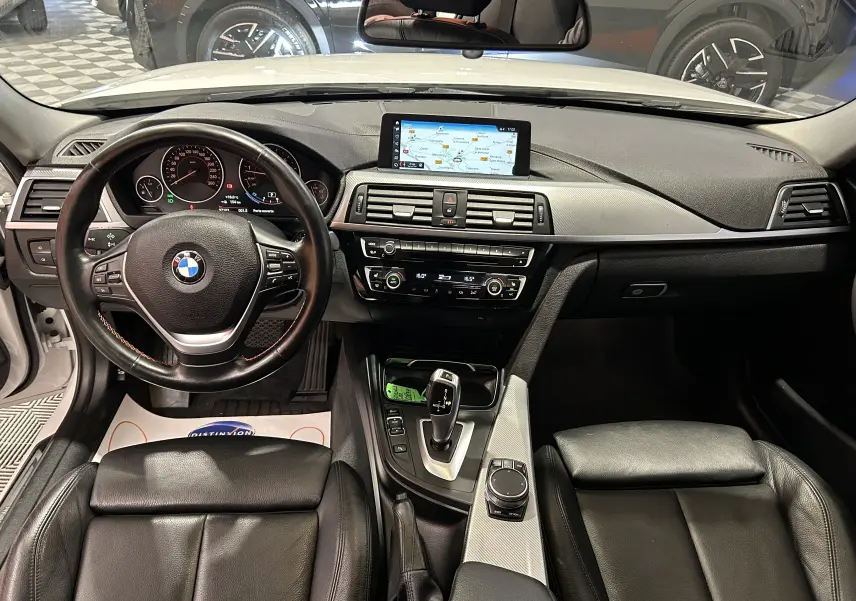 Vue intérieure avant de la BMW Série 3 320i 2018 avec tableau de bord noir, écran GPS et sièges cuir chauffants.