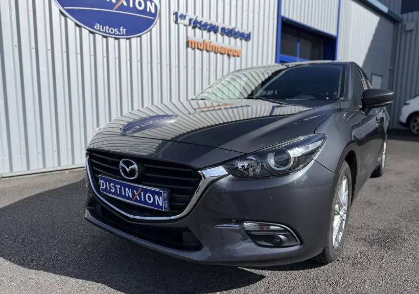 Vue 3/4 avant droite d'une Mazda3 gris métallisé 2017 avec calandre noire et phares LED visibles.